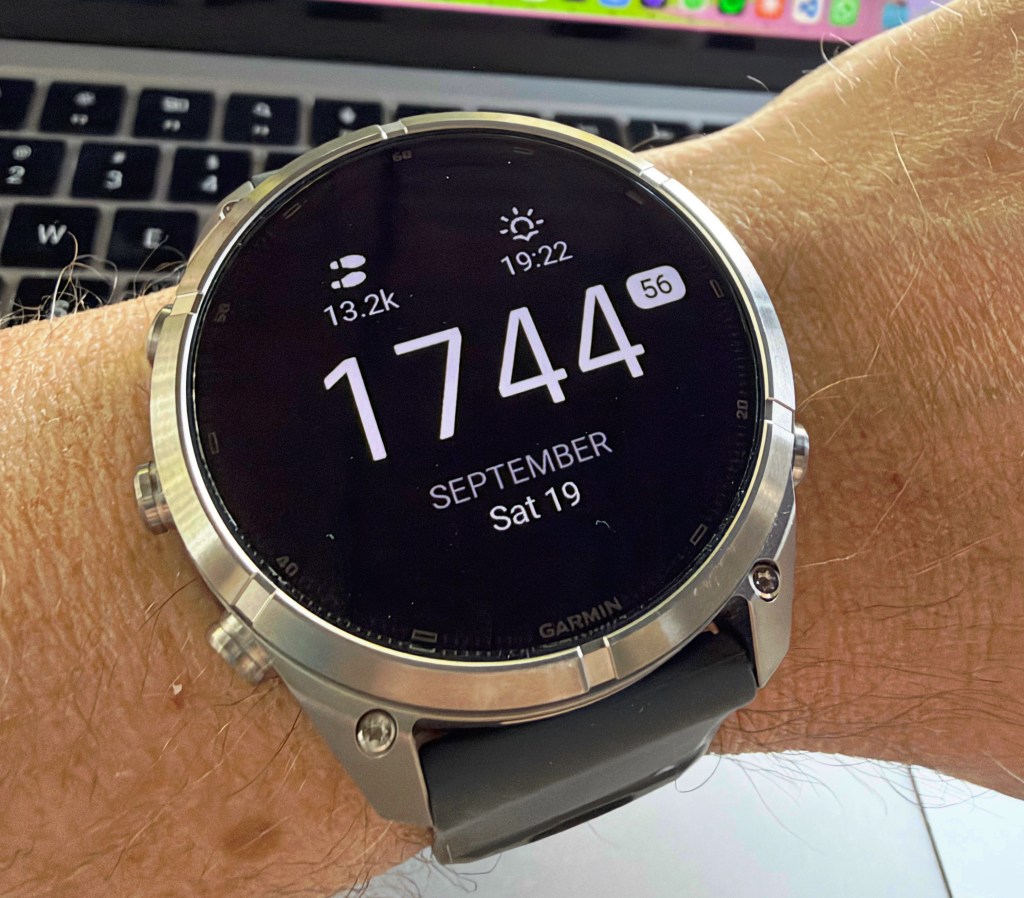 A close-up of a Garmin smartwatch displaying the time as 17:44, with the date showing September 19. The watch is being worn on a wrist with light skin and hair, placed against a blurred background of a laptop keyboard.