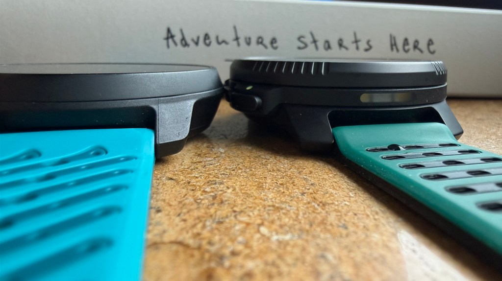 Close-up of two smartwatches side by side on a wooden surface, featuring turquoise straps and a message in the background that reads 'Adventure starts HERE'.