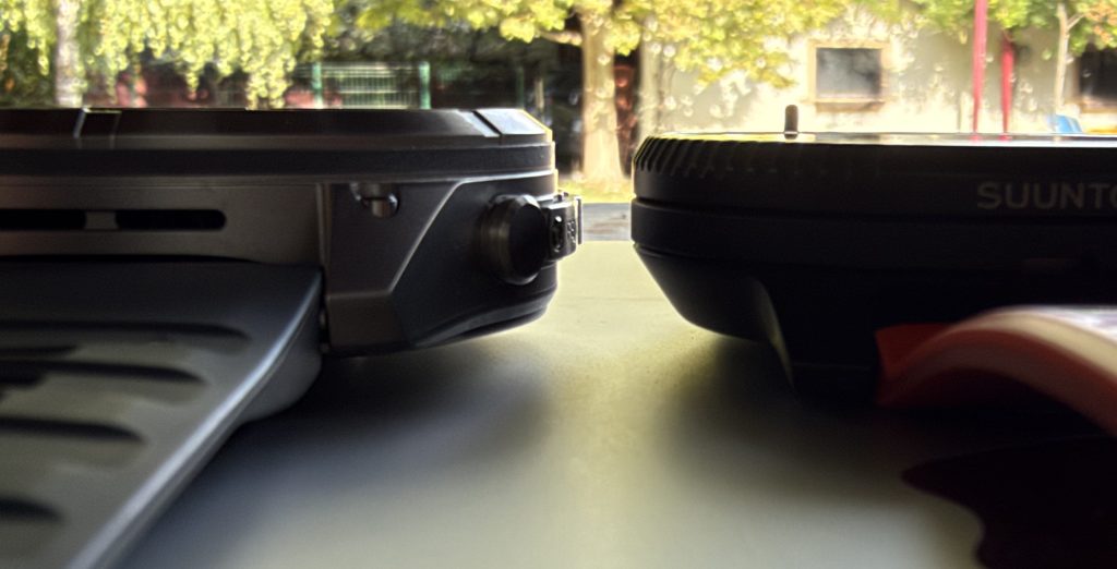 Close-up side view of a laptop and a smartwatch on a table, with a blurred background showing trees and a building.